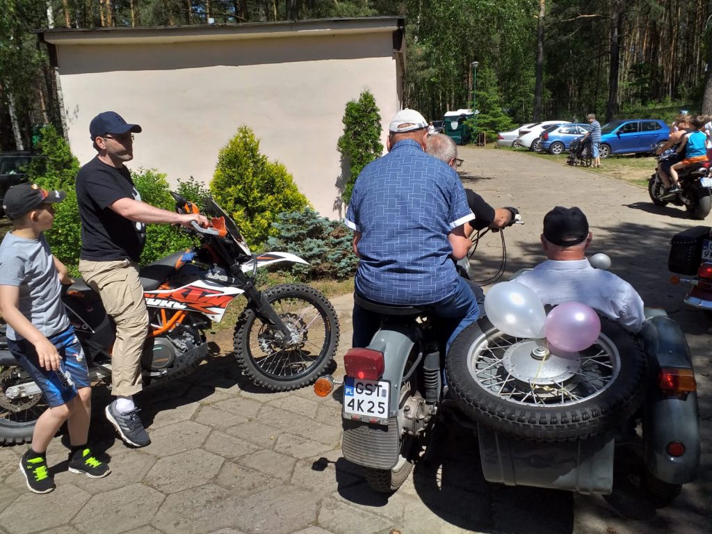 Ujęcie ukazuje 3 motory na jednym z nich mieszkańcy domu siedzą na motorze z dostawką gotowym do jazdy.