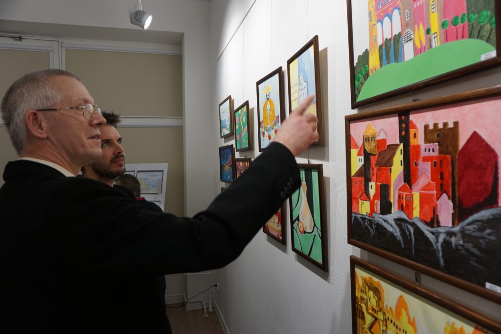 Jeden z artystów stojący przy obrazach i pokazujący palcem do gościa.
