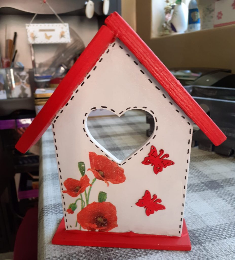 Drewniana ozdoba domku z wyciętym w środku sercem i namalowanymi czerwonymi różami oraz daszkiem