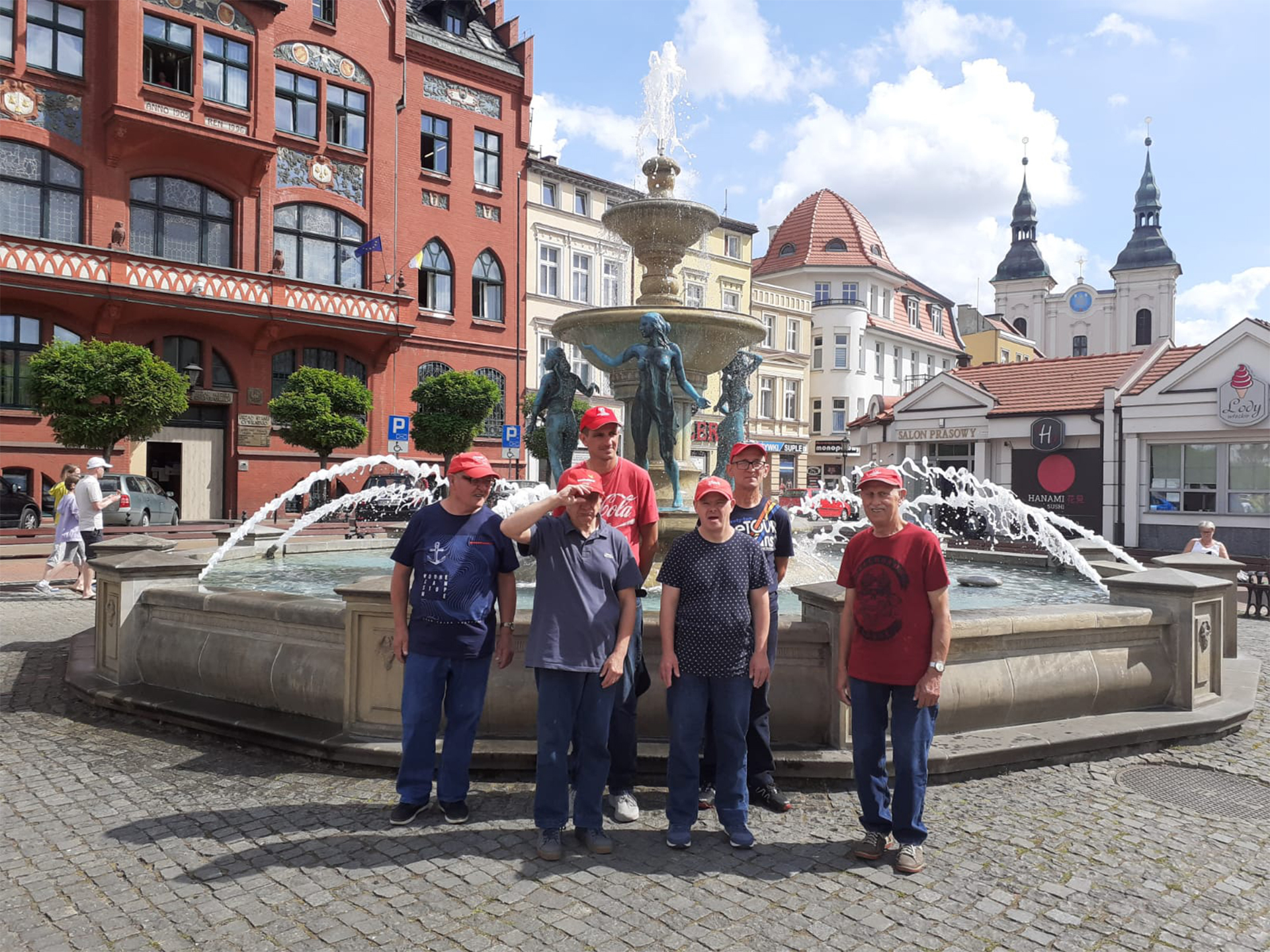Sześciu mieszkańców stoi przy fontannie na rynku w Chojnicach. W tle piękne stare wysokie kamienice
