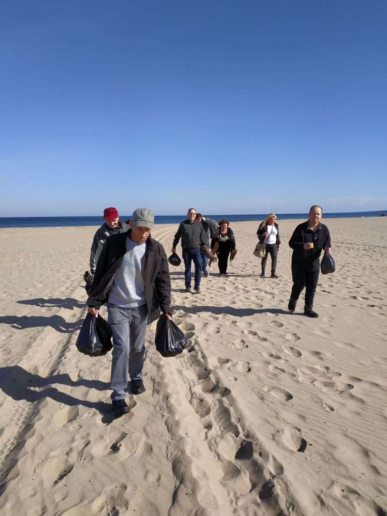Grupa osób idąca po piaszczystej plaży w rękach niosą czarne worki