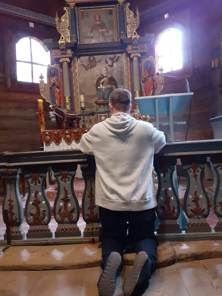 Mieszkaniec klęczący przed ołtarzem i Świętymi figurkami