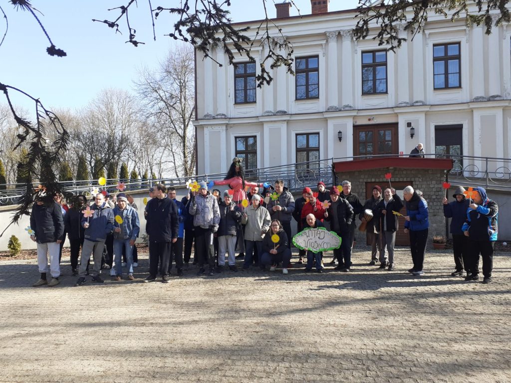 Grupa mieszkańców z opiekunami stojąca przed główną siedzibą - Pałacem