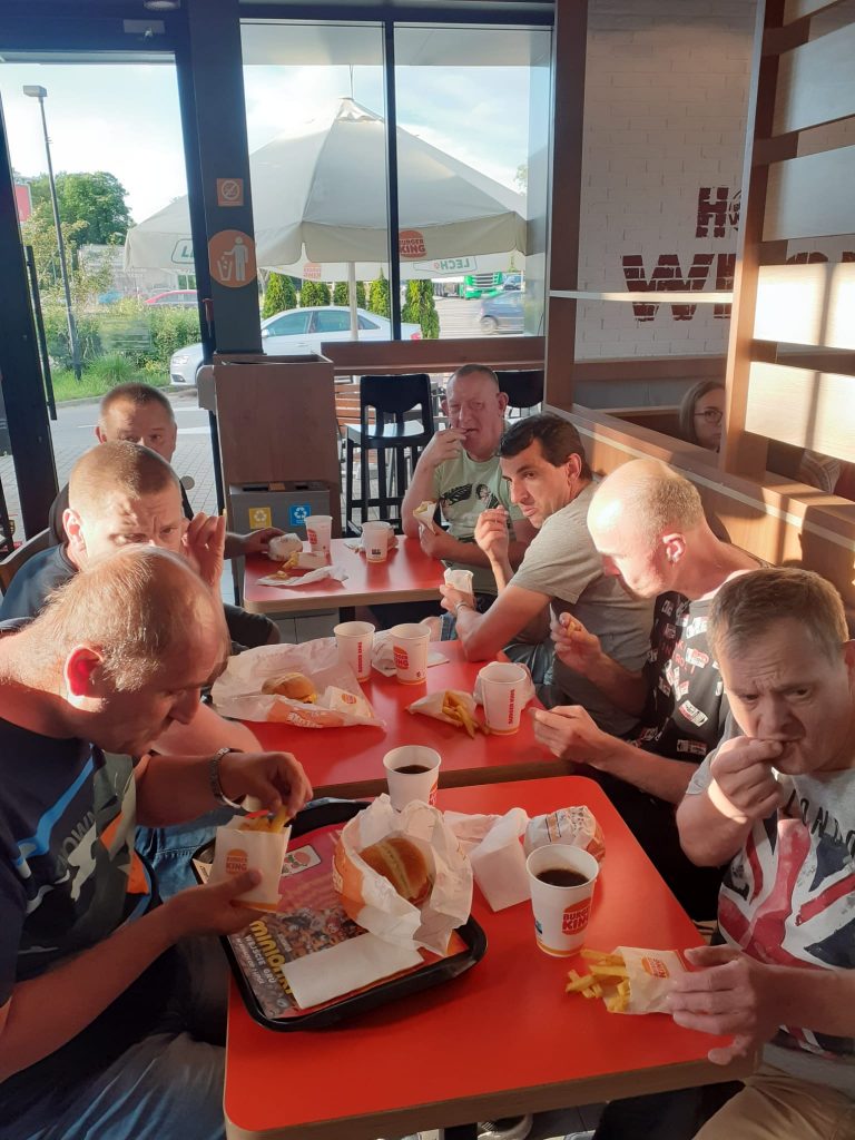 Podopieczni spożywający posiłek w Burger Kingu. Siedzą przy stołach i jedzą oraz piją kawę.