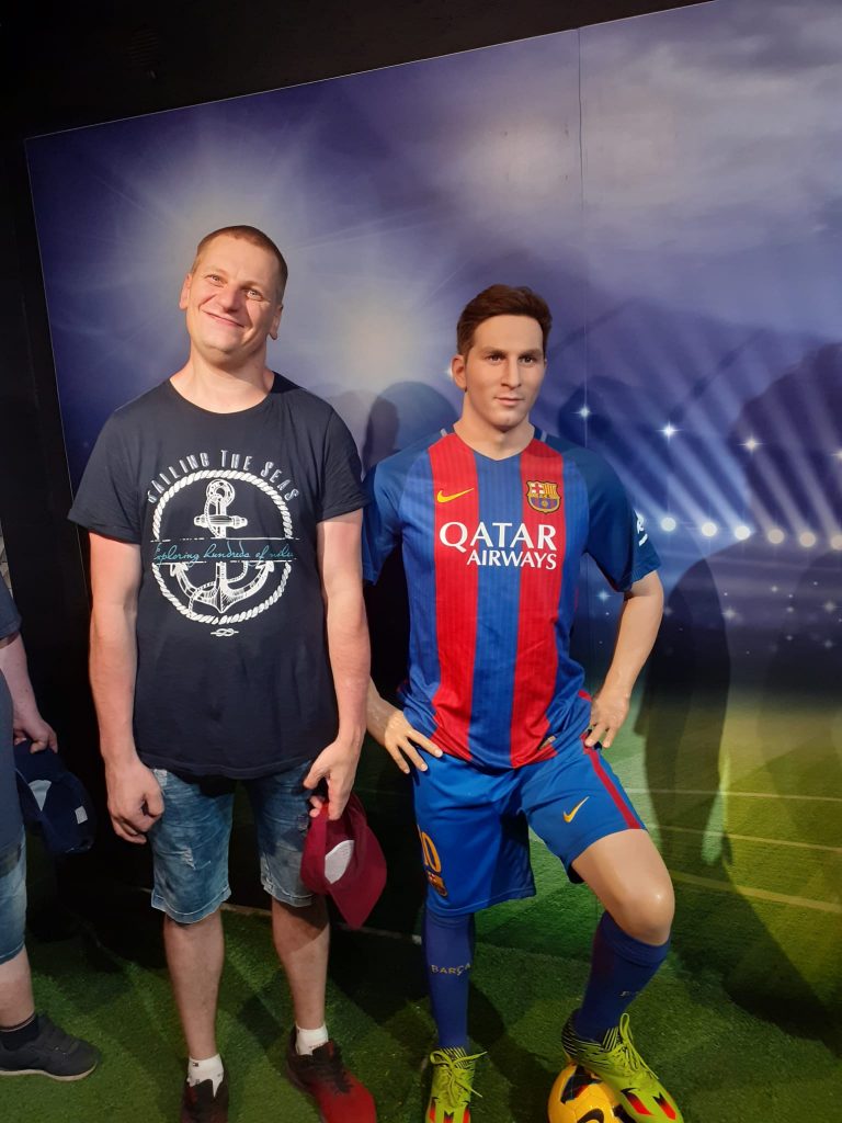 Uśmiechnięty mieszkaniec stoi obok figury woskowej Lionela Messiego. Leo ubrany w koszulce Barcelony, jedną nogę trzyma na piłce.