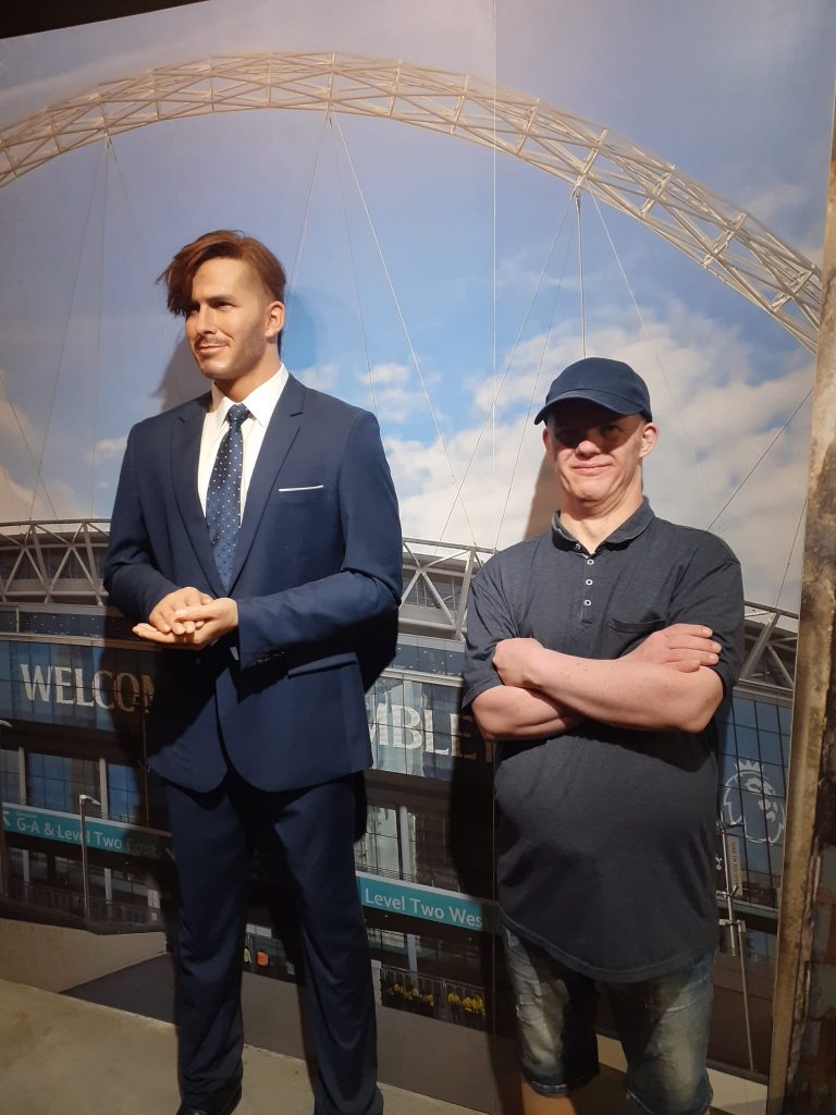 Mieszkaniec stoi z założonymi rękoma obok figury woskowej Davida Beckhama.