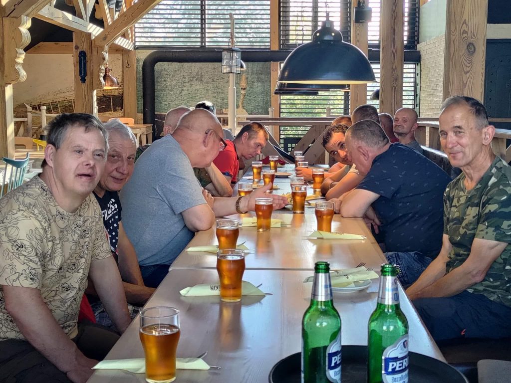 Grupoa mężczyzn siedzi przy stole w restauracji Manekin - czeka na posiłek. Na stole stoi bezalkoholowe piwo.