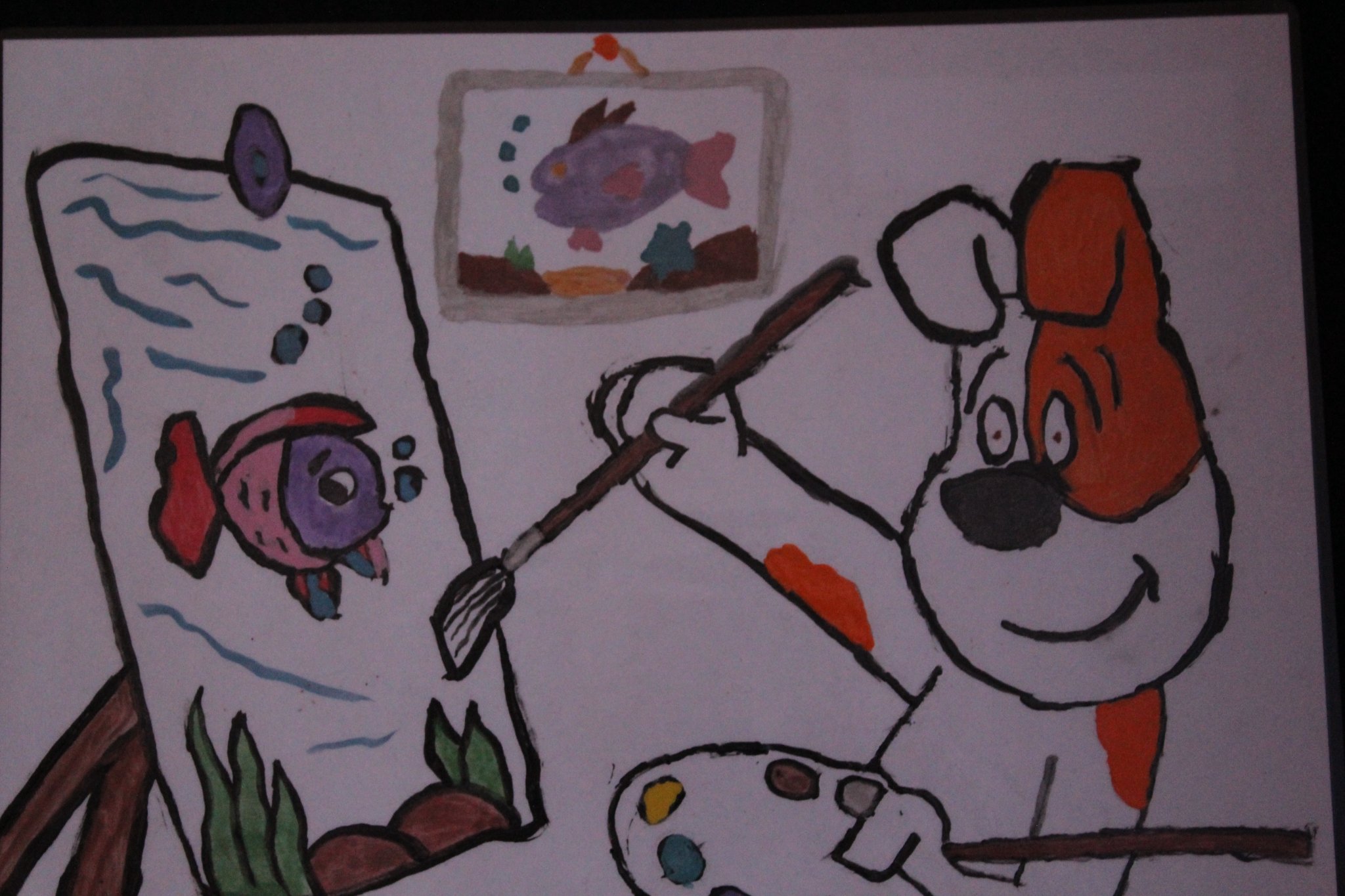 Pies "Reksio" maluje pędzlem na sztaludze obraz pływającej ryby. W tle obraz ryby.