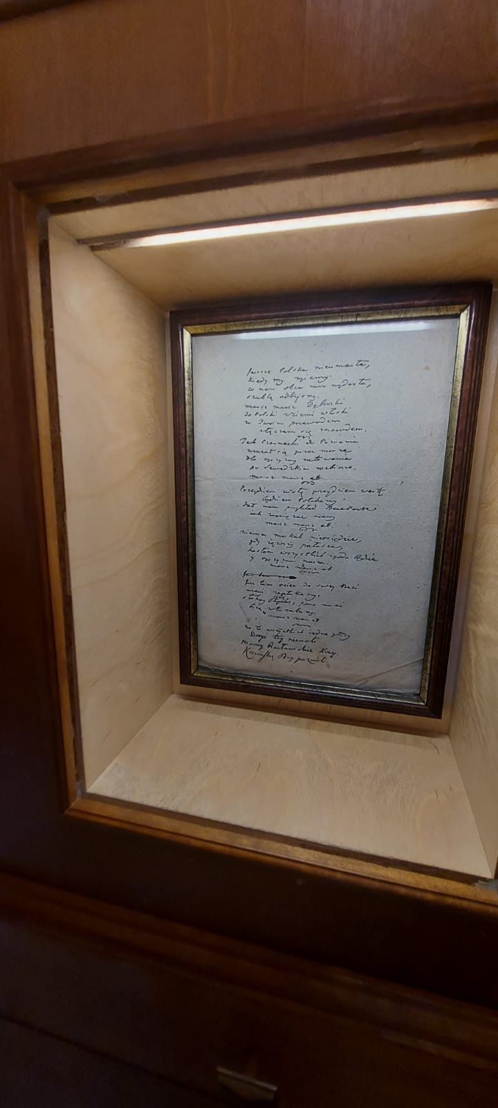 Odręczne pismo umieszczone w obrazie wisi w gablocie na ścianie.
