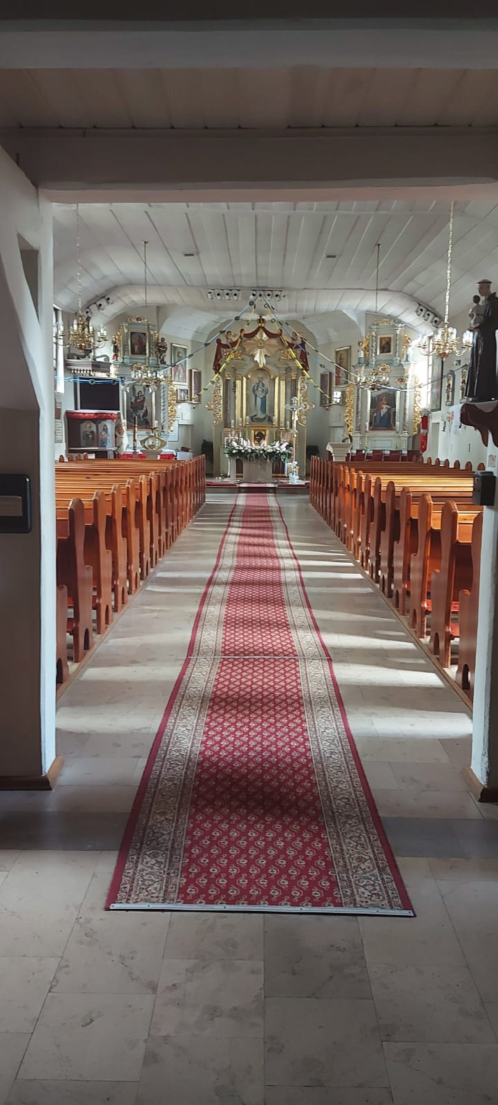 Drewniane ławki po obu stronach, a na środku pozłacany ołtarz kościoła obok niego święte obrazy.