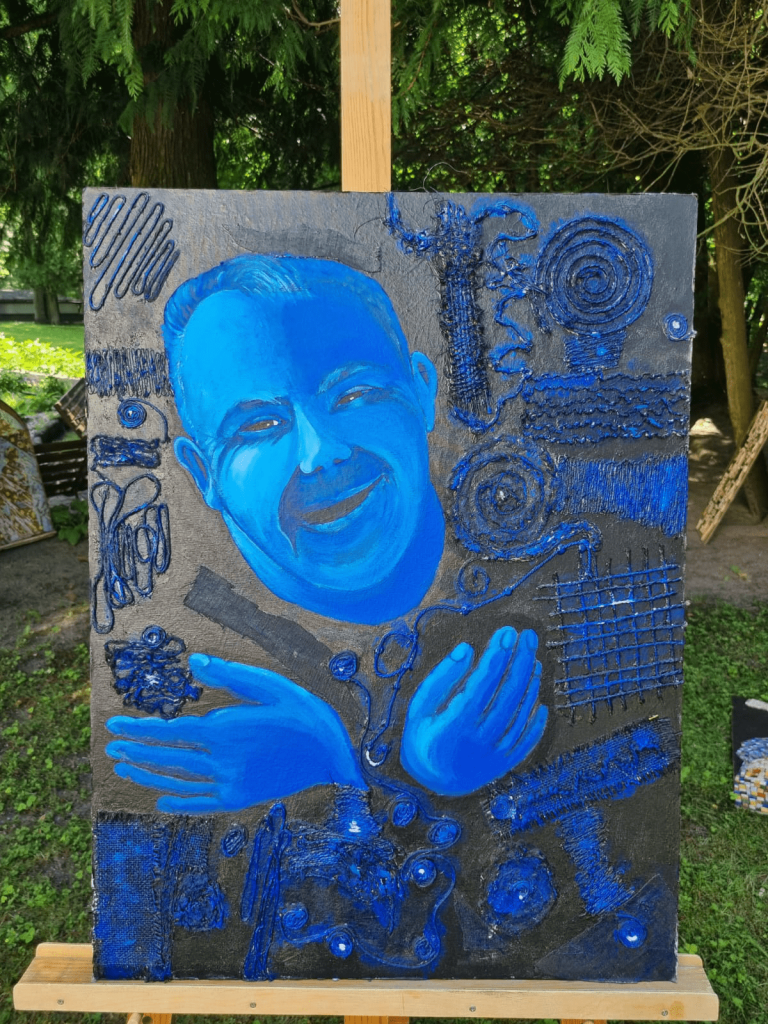 Niebieska twarz oraz ręce uśmiechniętego mężczyzny na obrazie, który stoi na stelarzu na dworzu.