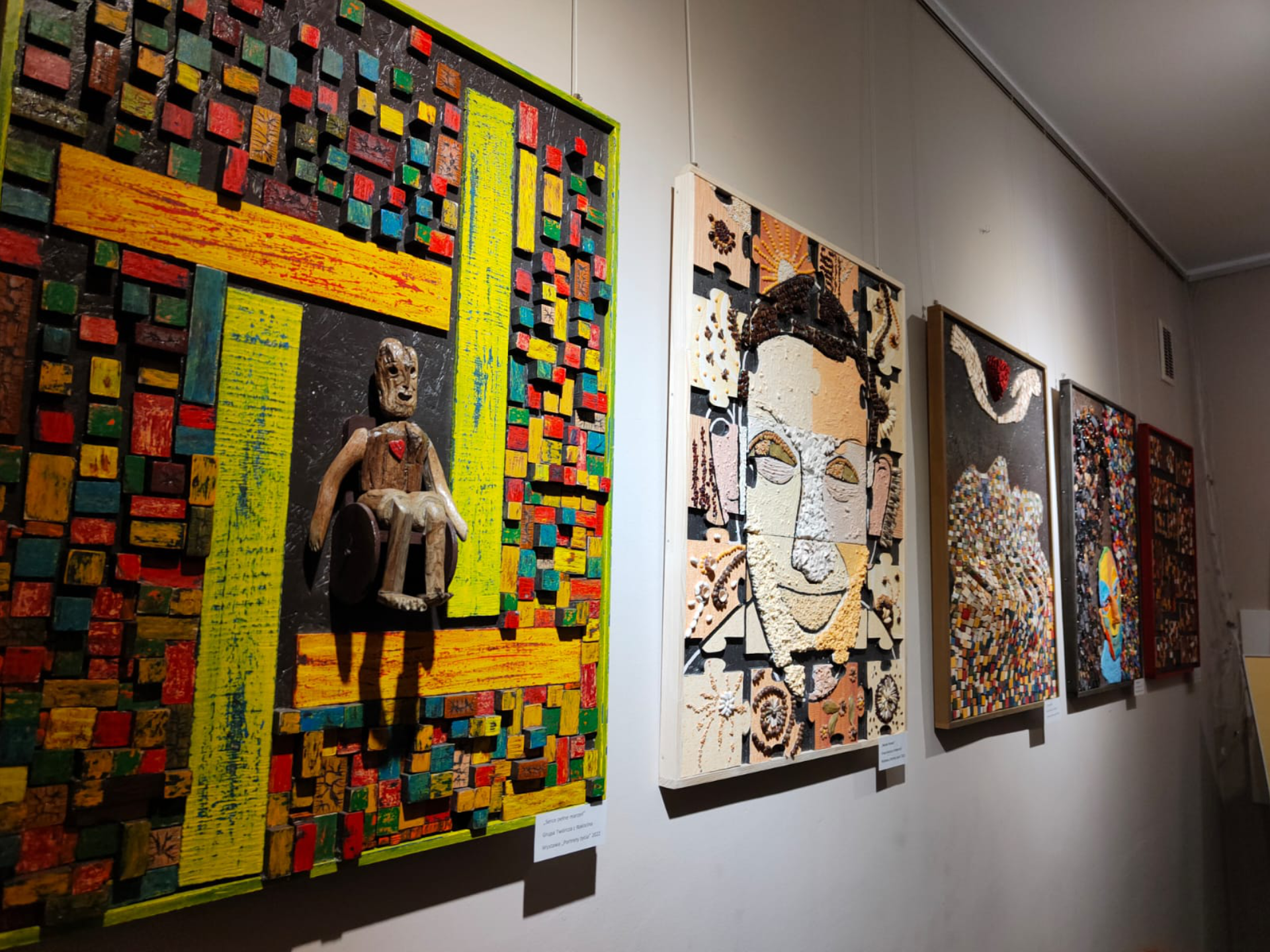 Cztery kolorowe obrazy powieszone na ścianie w Muzeum, wykonane ze sklejki, różnych kolorowych elementów np. muszli, koralitów.