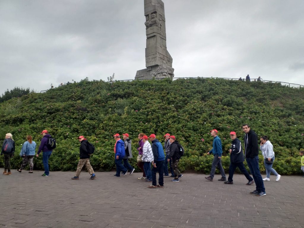 Grupa osób idących razem. W tle pomnik Westerplatte.