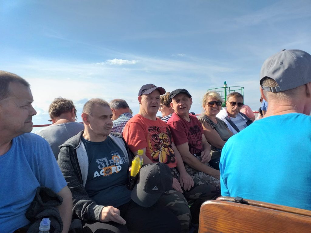 Grupa ludzi oraz paru mieszkańców siedzących wspólnie na statku.