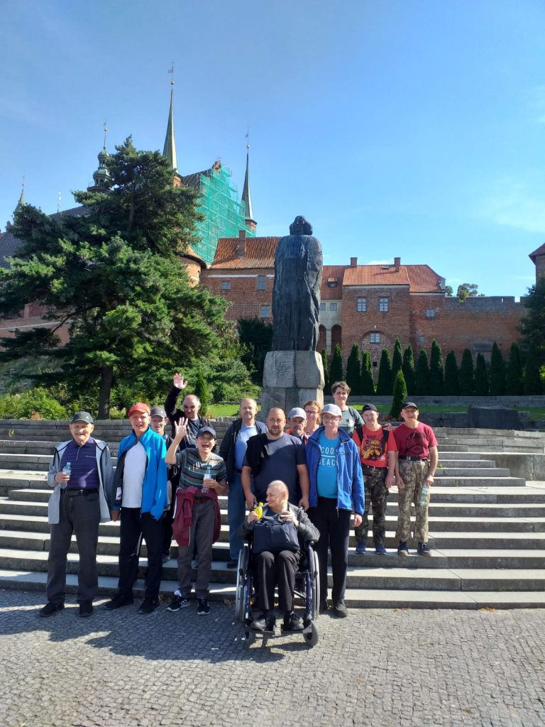 Uczestnicy wycieczki stojący na schodach przy pomniku Kopernika nieopodal Domu Kopernika.