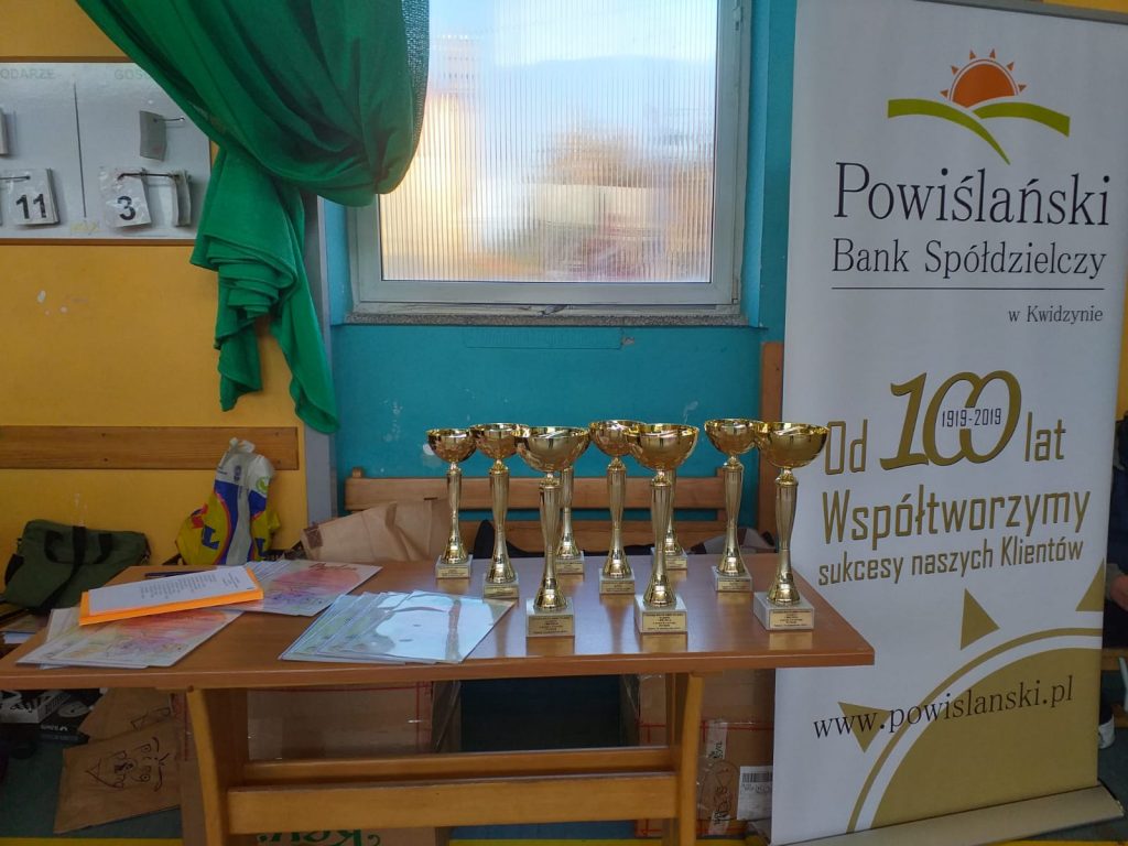 Na drewnianym stole stoi 9 złotych pucharów przyznawane zwycięzcom swoich grup od 1 do 3 miejsca.