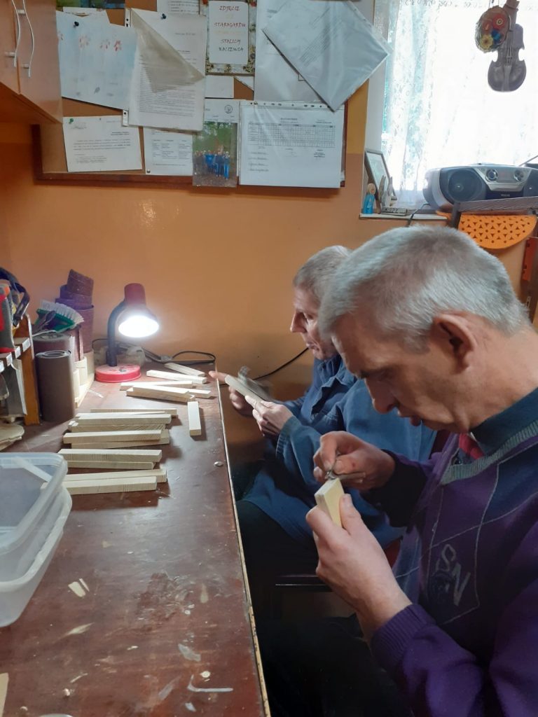 Dwóch podopiecznych siedzących w pracowni, szlifuje drewniane elementy