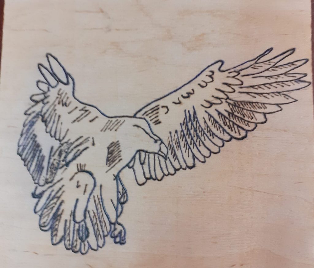 Wypalanka w drewnie przedstawia ptaka z rozłożonymi skrzydłami