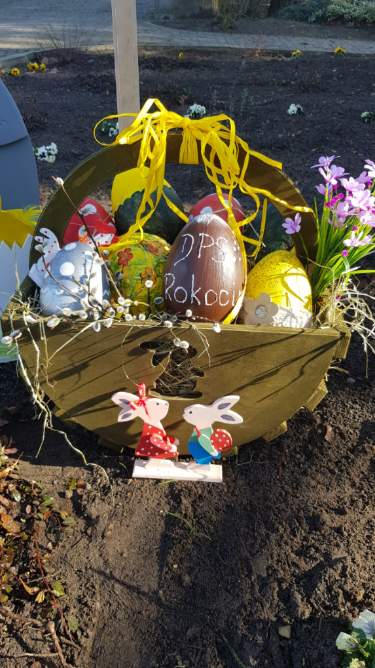 Drewniany koszyk wypełniony ozdobami, kolorowymi jajkami oraz kwiatami