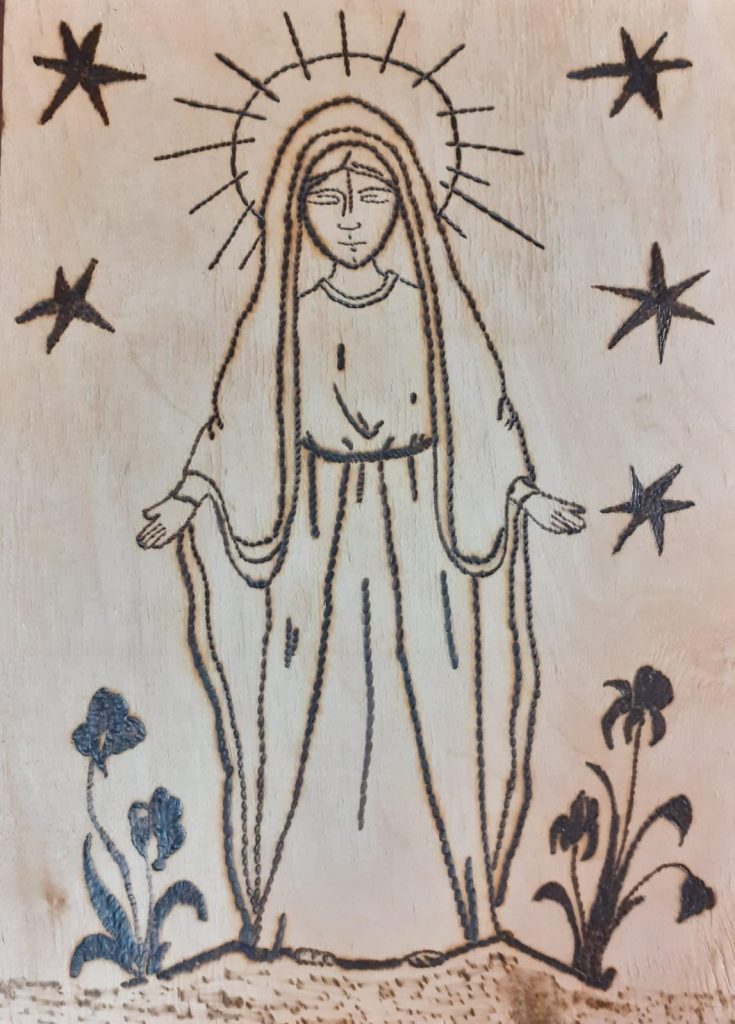 Wypalanka w drewnie przedstawia Matkę Boską wokół niej gwiazdy, a na ziemi po obu stronach kwiaty