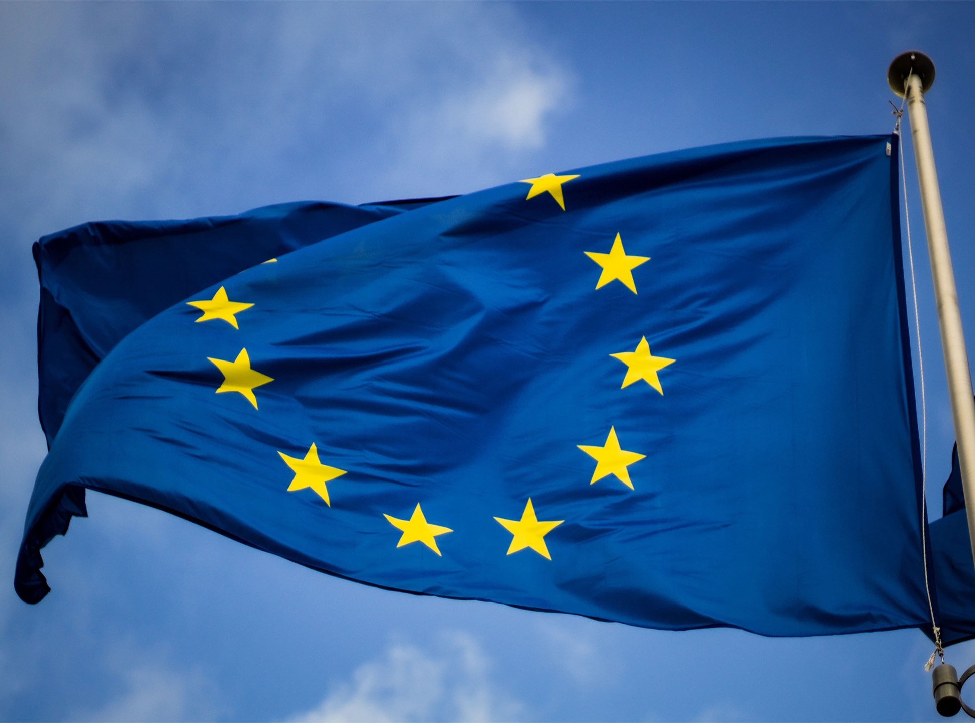 Flaga Unii Europejskiej (Niebieska flaga z żółtymi gwiazdami w kółku) powiewa na wietrze.