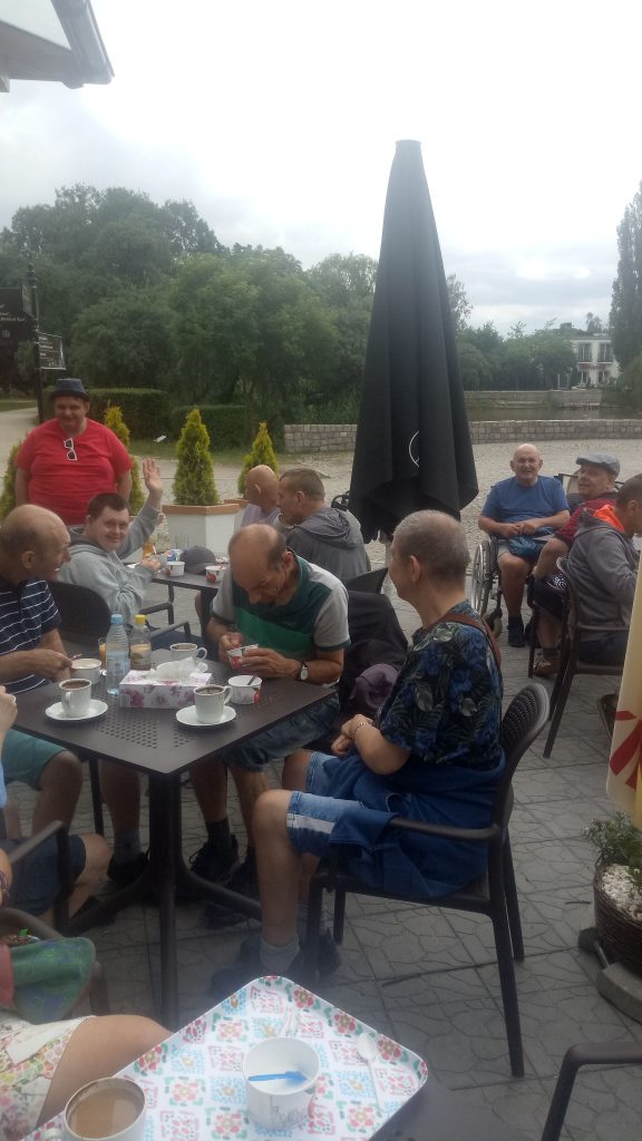 Grupa osób siedząca przy stolikach, pijąca kawę i jedząca lody.