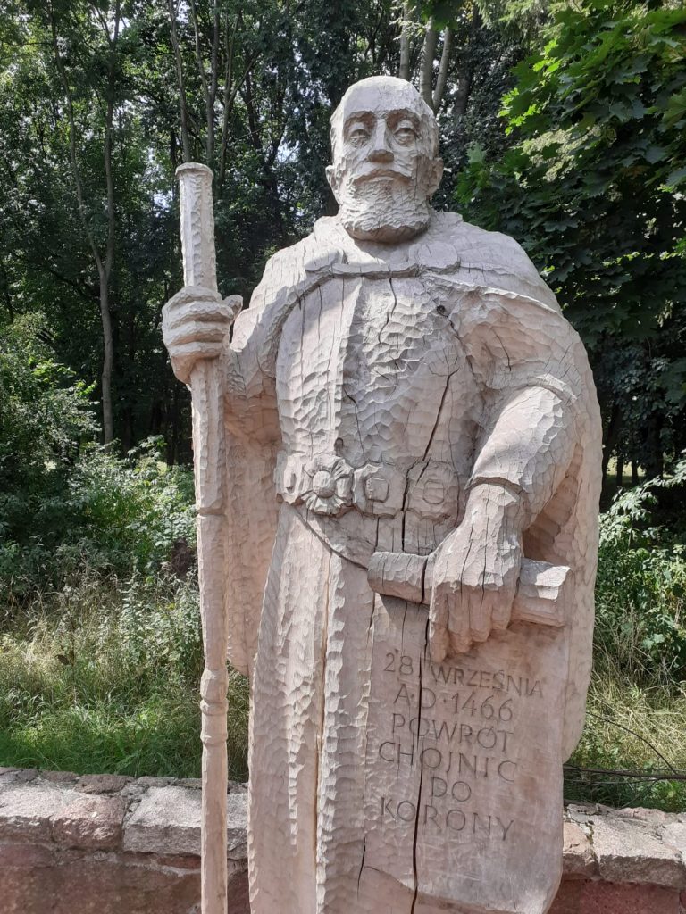 Drewniany posąg Hetmana Polskiego trzymającego laskę oraz zwój na którym jest napisane "28 Września A.D. 1466 Powrót Chojnic do Korony"