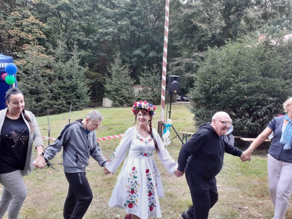 Kobieta z zespołu folklorystycznego ubrana w barwy Kociewia trzyma się za ręce i tańczy z mieszkańcami
