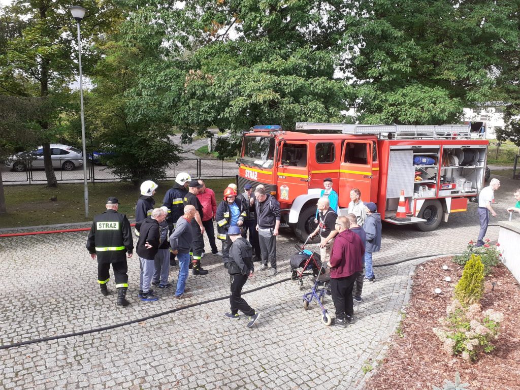 Wóz strażacki na podjeździe do siedziby Domu a przy nim strażacy oraz zainteresowani podopieczni Domów.