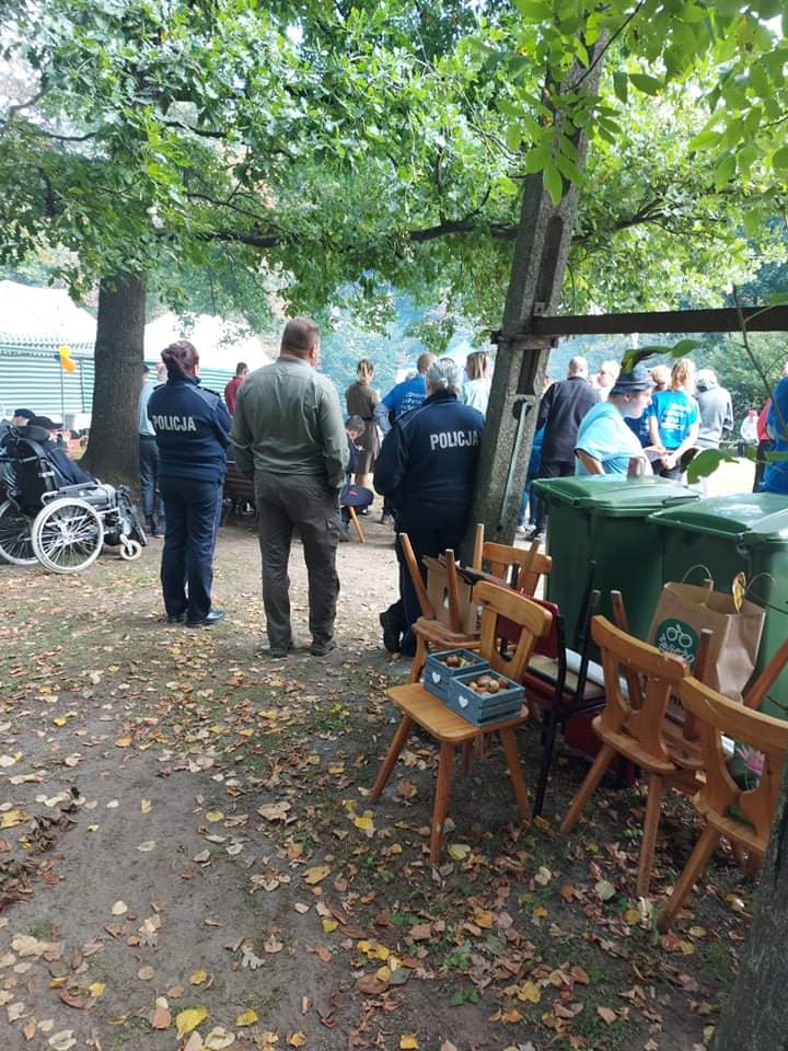 Dwie policjantki stoją z boku drzewa wpatrują się w tłum ludzi.