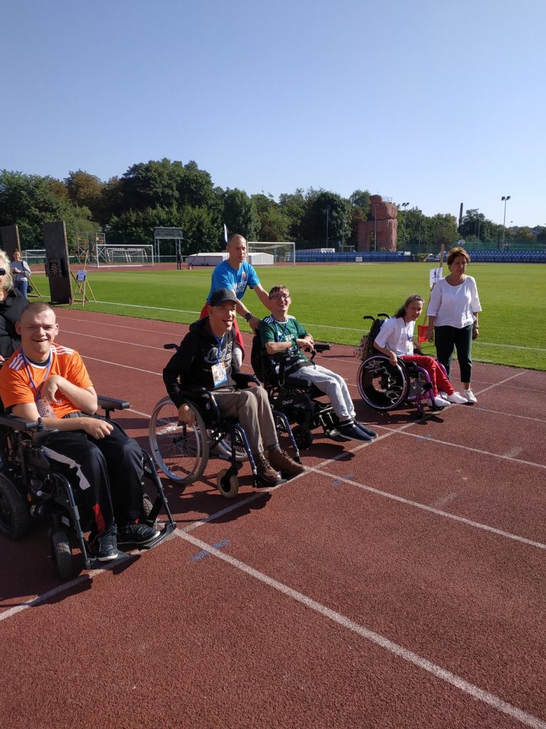 Osoby na wózkach inwalidzkich ustawione są obok siebie na bieżni na stadionie miejskim.