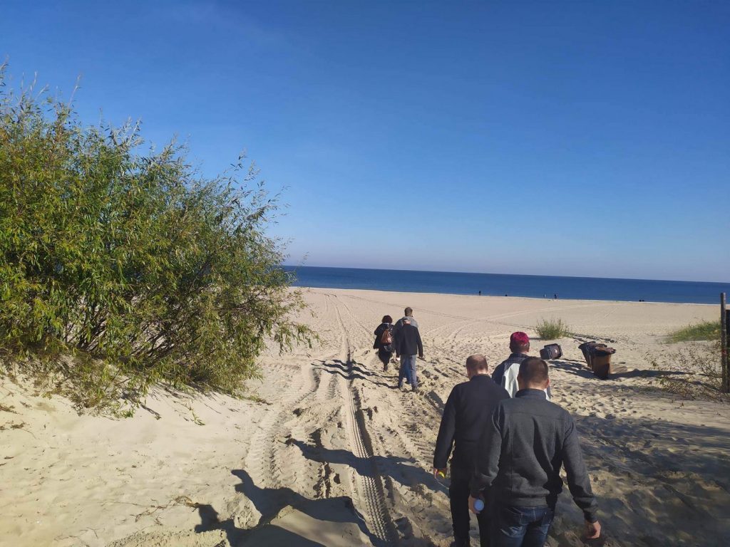 Grupa osób wchodząca na plaże, wszyscy idą po piasku w stronę morza