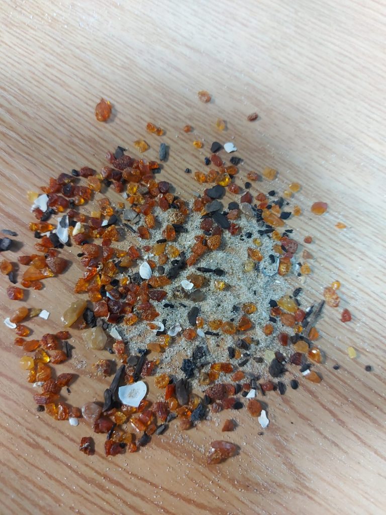 Kawałki małych bursztynów z nadmorskim piaskiem rozrzucone na stole