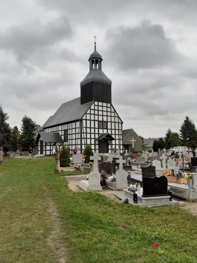 Mały kościół z wieżą na, której jest krzyż, przed kościołem mały cmentarz z nagrobkami
