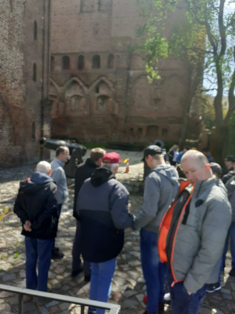 Grupa mieszkańców stojąca przy murach zamku.
