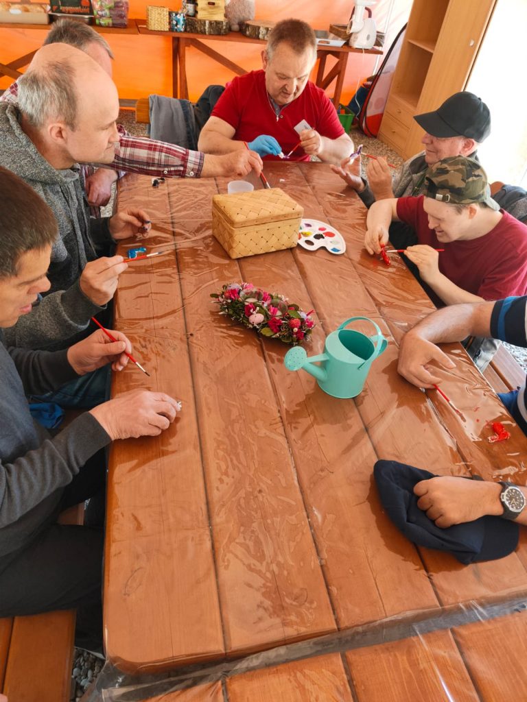 Grupa mężczyzn podczas malowania farbami małych drewnianych figurek z drewna.