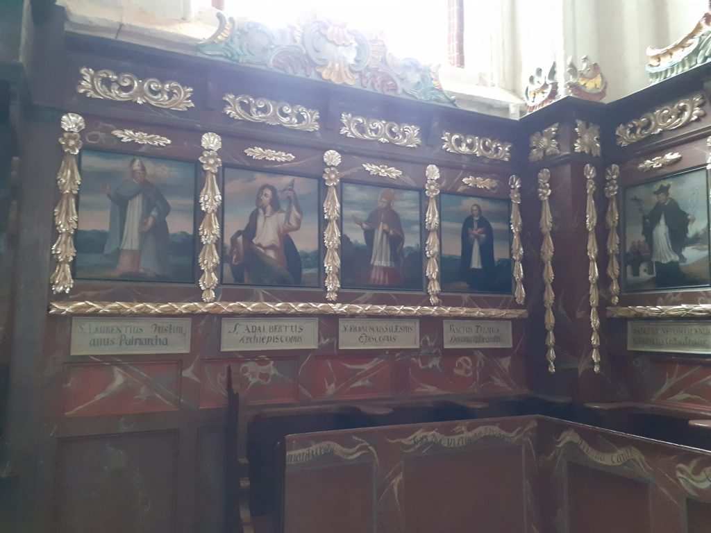 Ściana z obrazami świętych, w koło obrazów złote rzeźbienia.