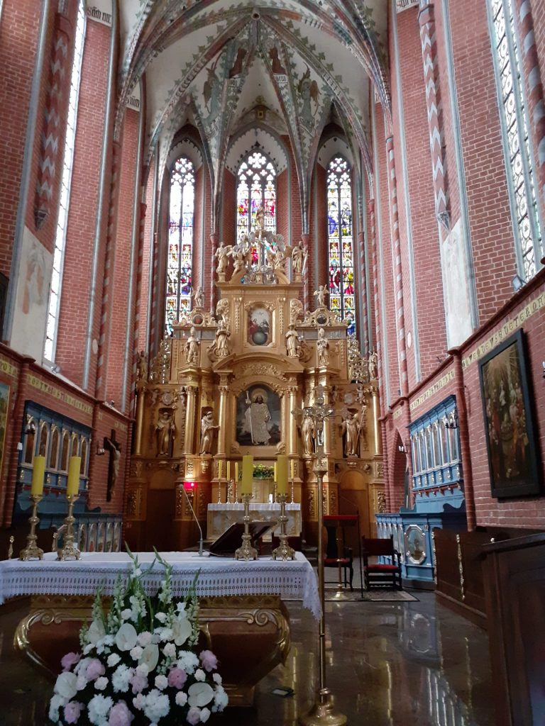 Złoty ołtarz w kościele, święte obrazy oraz wysokie okna z witrażami pod same sklepienia.