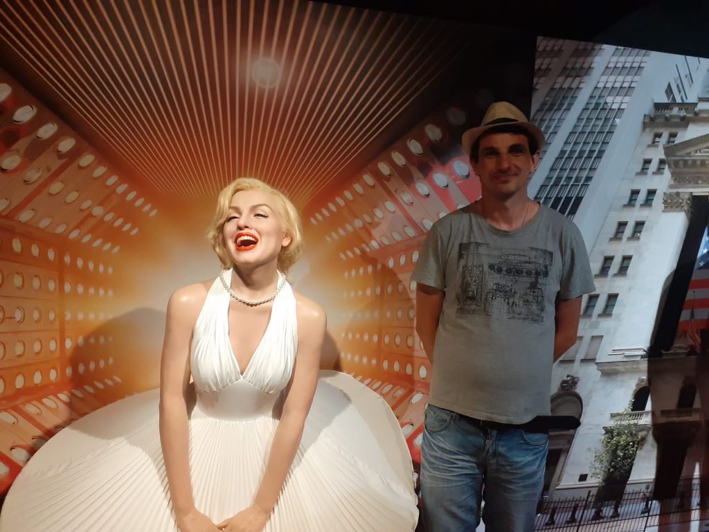 Mieszkaniec z kapeluszem na głowie stoi obok figury woskowej Marilyn Monroe.