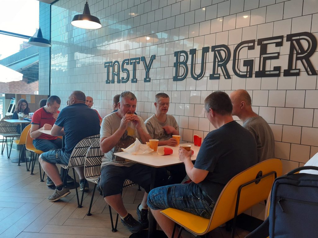 Ośmiu podopiecznych siedzących przy dwóch stolikach podczas jedzenia burgerów, frytek i picia kawy.