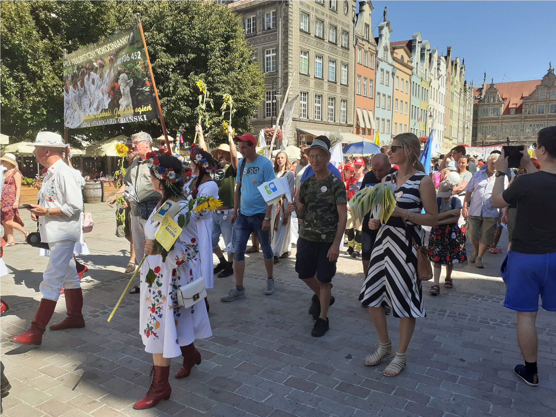 Korowód osób idących wspólnie ulicami Gdańska. Wielu z nich trzyma chorągiewki, a niektórzy transparenty.