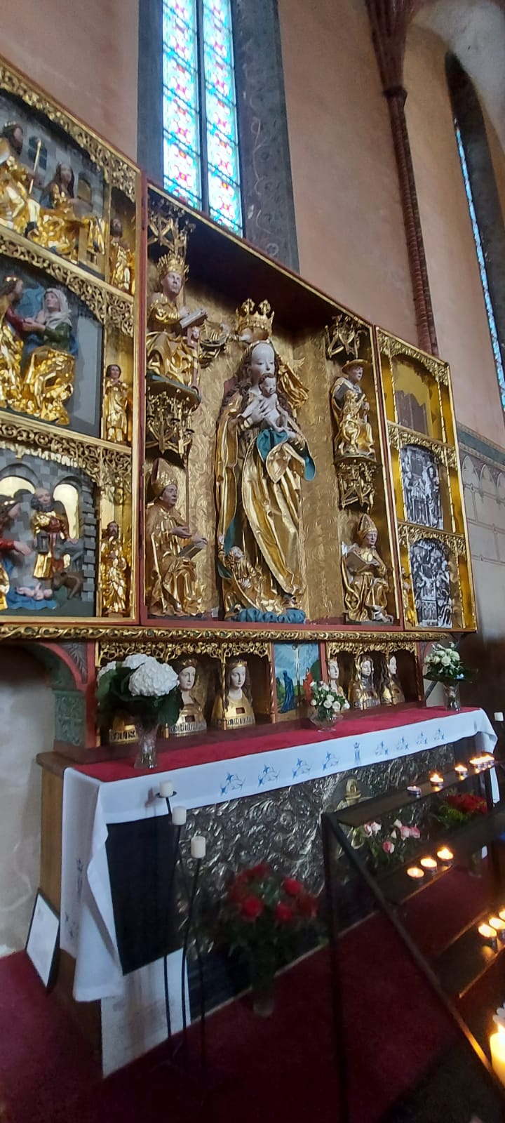 Złoty ołtarzyk z figurkami świętych. Po nim świece oraz kwiaty