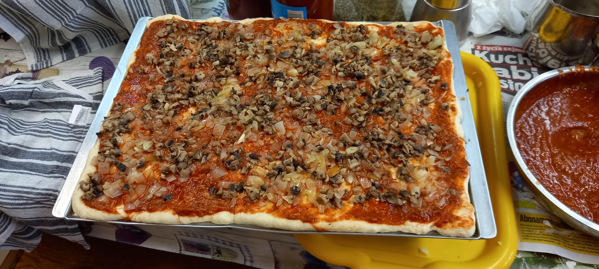 Na szerokiej metalowej blaszce leży duża przygotowana do spożycia pizza.