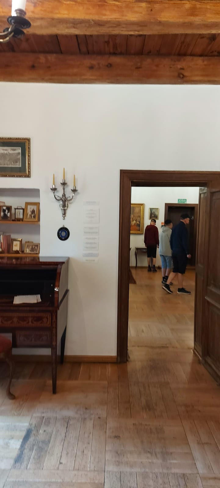 Trzech mężczyzn w pomieszczeniu Muzeum widoczni w pokoju obok.

