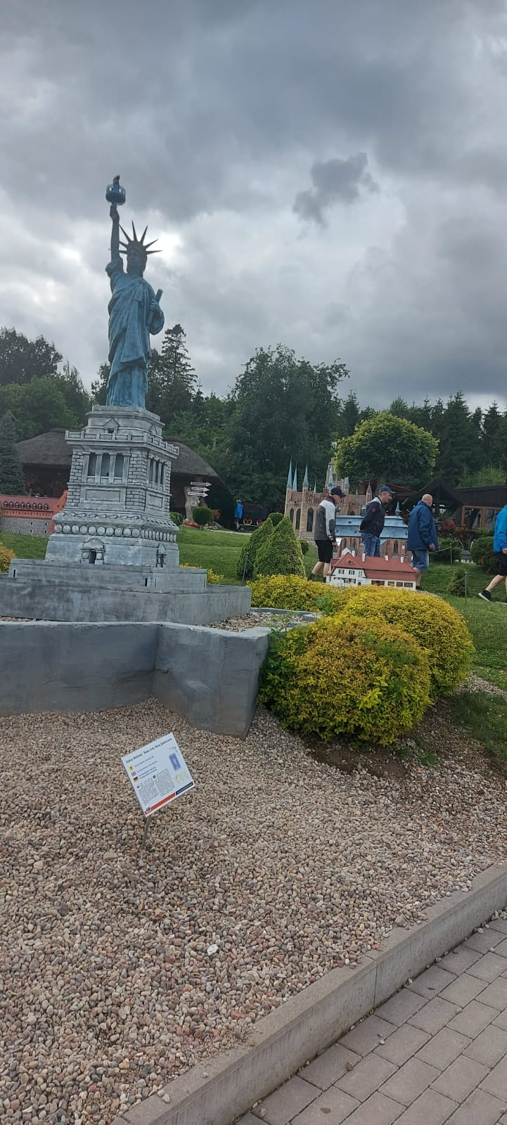Miniaturowa rzeźba statuy Wolności w tle mieszkańcy idący przy innych rzeźbach.
