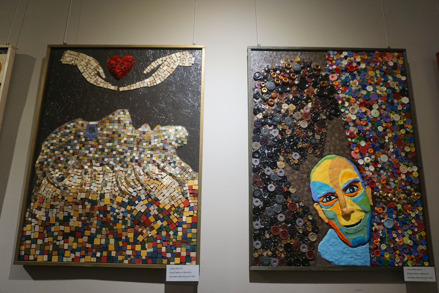 Dwa kolorowe obrazy na ścianie. Po lewej wykonany z małych kolorowych drewnianych elementów, twarz nad nią ręce trzymające serce. Po prawej kolorowa głowa między guzikami.