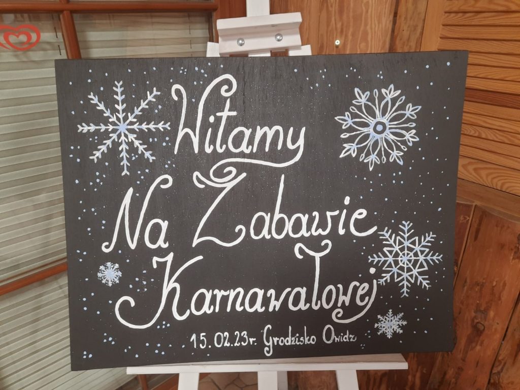 Napis na drewnianej tablicy "Witamy na zabawie karnawałowej 15.02.2023 Grodzisko Owidz".