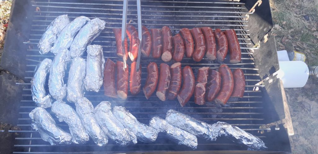 Grill na, którym leżą zawinięte kaszanki oraz leżą kiełbaski.